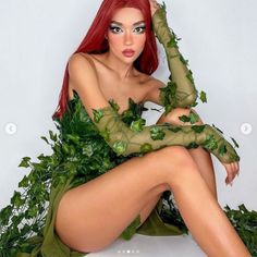 a woman with red hair sitting on top of a white toilet covered in green leaves