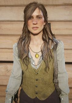 a woman with long brown hair wearing a green vest and necklace standing in front of a wooden wall