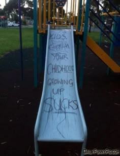 a slide with graffiti written on it in a park area next to a play structure