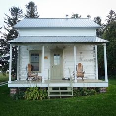 two chairs sit on the porch of a small white house