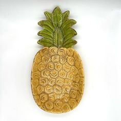 a wooden pineapple with green leaves on it's back and sides, against a white background