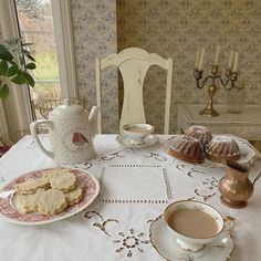 a table topped with cookies and cups of coffee next to a tea pot on top of a white table cloth