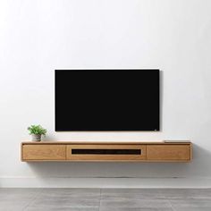 a flat screen tv sitting on top of a wooden shelf next to a potted plant