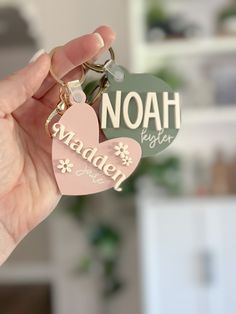 a hand holding two heart shaped keychains that say noah, made in heaven