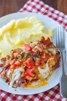 a white plate topped with meat covered in sauce and vegetables next to mashed potatoes