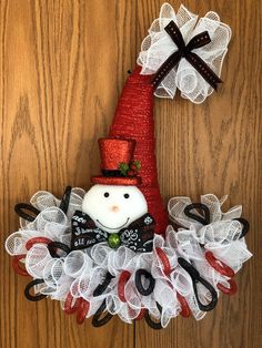 a christmas wreath with a snowman on top and ribbons around the bottom, hanging on a wooden door