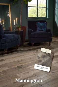 A moody living room with dark green walls and dark blue velvet chairs with lit candles that features the Mannington Hardwood pattern, Triumph and a swatch of the floor Hardwood Plank Flooring, Hickory Flooring, Emser Tile, Floating Floor, Low Pile Carpet, Stair Nosing, Engineered Flooring, Tile Trim, Stacked Stone