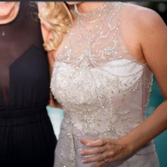 two women standing next to each other in formal wear and one is holding a drink