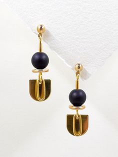 These earrings are sleek and modern, crafted from golden brass and semi precious stone.  The matte, black onyx stone features among the geometric shapes, an elongated semi-circle, layered with a solid brass oval hangs below, adding a touch of contrast and sophistication to the overall design.  The combination of geometric shapes, the matte black stone, and the metallic shine creates an elegant, minimalist aesthetic. A brass ball stud with stainless steel post holds the design from the top.  Approximate measurements- 4.5cms long 1.5cms wide All Set Theory jewellery comes with care instructions and a polishing pad to keep your jewellery looking shiny and fabulous! ✨ Set Theory, Black Statement Earrings, Dangle Earrings Gold, Gold Dangle Earrings, Stone Feature, Black Onyx Stone, Earrings Geometric, Steel Post, Earrings Unique