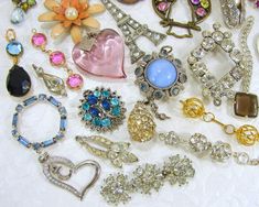 an assortment of jewelry is displayed on a white tablecloth with flowers and brooches