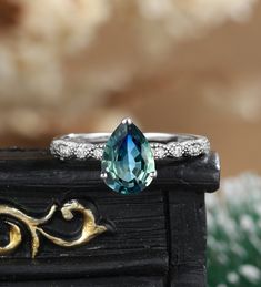 a ring with an aqua blue stone and diamond accents sits on top of a piece of wood