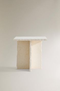 a small white table sitting on top of a floor next to a chair and wall