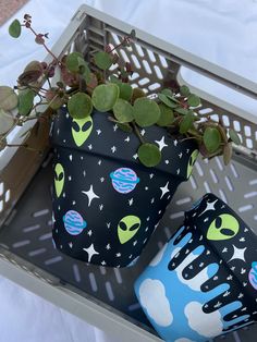 two pots with plants in them sitting on a table next to a planter that has planets and stars painted on it