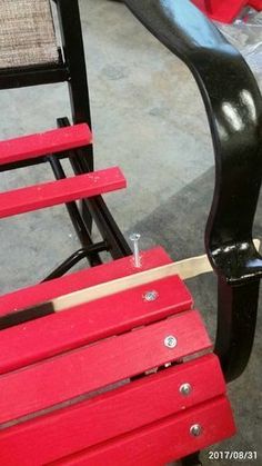 a red chair sitting on top of a cement floor next to a black bench with a wooden slatted back