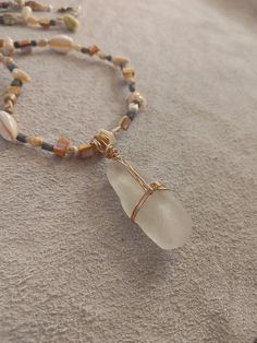 a beaded necklace with a glass pendant on it's end, sitting on the sand