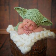 a newborn baby wearing a green hat and sleeping in a wooden bucket filled with white balls