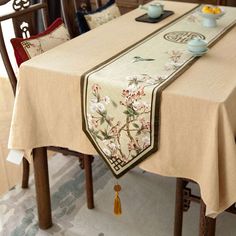 a dining room table covered with a beige tablecloth and two tea cups sitting on top of it