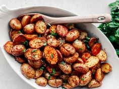 a white bowl filled with potatoes and parsley on top of a table next to a wooden spoon