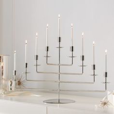 a white table topped with a large metal candle holder filled with lit candles next to a mirror