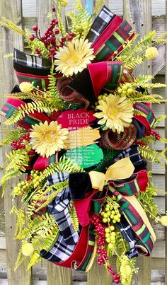 a wreath with yellow flowers and red ribbon hanging on the side of a wooden fence