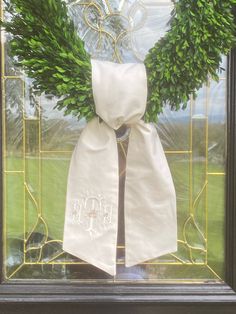 a green wreath on top of a window with a white ribbon hanging from it's side