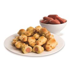 a white plate topped with pigs in a blanket next to a bowl of hot dogs