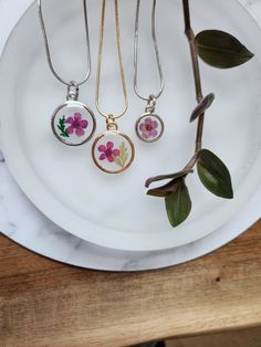 three necklaces are sitting on a plate next to a flower branch and some leaves