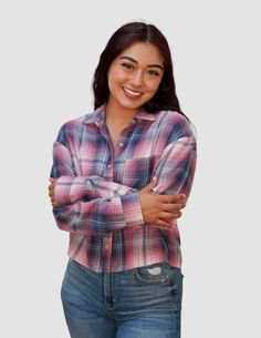 a woman with her arms crossed standing in front of a white background wearing jeans and a plaid shirt