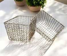 two metal baskets sitting on top of a white table next to potted planters