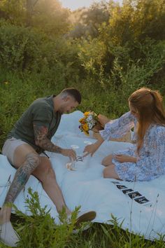 a man and woman sitting on a blanket in the middle of a field eating food