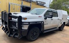 a white truck is parked in front of a yellow building with other trucks behind it