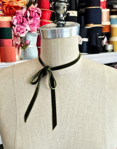 a mannequin with a green ribbon on it's neck and flowers in the background