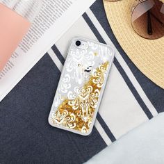 a white and gold iphone case sitting on top of a beach towel next to sunglasses