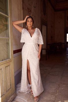 a woman in a white dress leaning against a wall