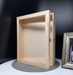 an empty wooden box sitting on top of a table next to a framed photo and a silver frame