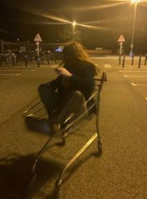 a woman sitting in a shopping cart on the side of the road at night time