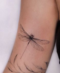 a woman's arm with a tattoo of a dragonfly on the left side