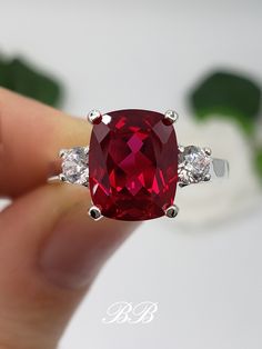 Made to order.  Please allow up to 3 weeks for the production of your selection. This listing is for a 925 non-plated sterling silver or non-plated gold three stone trellis ring with a high quality lab created ruby elongated cushion cut gemstone and high quality cubic zirconia diamond accent stones. Center Stone Gem Type: Lab Created Ruby Shape: Elongated Cushion Cut Size: 10x8mm Weight: 3.5 carats approximately Quality: AAA Hardness: 9 Mohs Accent Stones Gem Type: Lab Created Cubic Zirconia Diamonds Shape: Round Brilliant Size: (2) 3.5mm Color: White Quality: 6A Hardness: 8.5 Mohs Available in the following Metal Options (all metal are non-plated and solid) 925 Sterling Silver 10kt White Gold (non-rhodium plated) 10kt Yellow Gold 14kt White Gold (non-rhodium plated) 14kt Yellow Gold 14kt Classic Lab-created Ruby Jewelry For Promise, Classic Promise Jewelry With Lab-created Ruby, Elegant Lab-created Ruby Jewelry For Promise, Elegant Jewelry With Lab-created Ruby For Promise, Classic Red Jewelry For Promise, Classic Round Cut Lab-created Ruby Jewelry, Luxury Sterling Silver Ruby Ring For Formal Occasions, Sterling Silver Jewelry With Rectangular Center Stone, Sterling Silver Jewelry With Rectangular Prong Setting