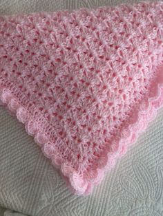 a pink crocheted blanket sitting on top of a bed