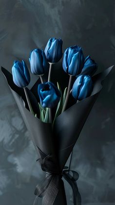 a bouquet of blue tulips is wrapped in black paper and tied with a bow