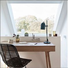 a desk with a chair, lamp and books on it in front of a window