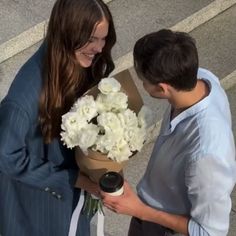 a young man holding a bouquet of white flowers next to a woman