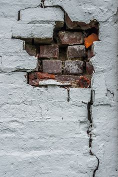 a white brick wall with a hole in the middle that has rusted paint on it