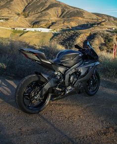 a black motorcycle parked on the side of a dirt road in front of a mountain