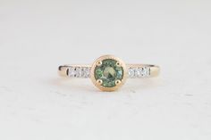 a green and white diamond ring sitting on top of a white surface with two diamonds around it