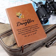 a brown book with the words to my daughter on it sitting next to a pair of binoculars