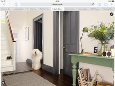 a white dog is standing in the hallway next to a green table and gray door