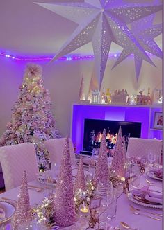 a dining room table set for christmas dinner with purple lighting and white trees on the wall