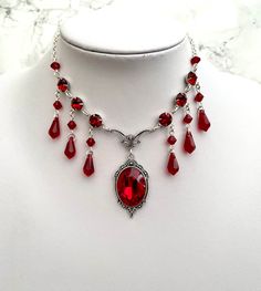 This regal looking necklace features a beautifully faceted glass jewel that promises to catch the eye as it sits in an elegant silver tone setting. The jewel is accompanied by an array of gorgeous glass drops and round faceted jewels.  There are 2 chain length options available: - Choker Length - 16" including a 5" chain extender. - Necklace Length - 20" including a 5" chain extender. Materials include; silver plated copper, silver plated brass, steel and high quality, precision cut glass from E Dark Regency, Kalung Aesthetic, Garnet Accessories, Gothic Items, Necklace Blood, Ruby Choker, Diy Statement Necklace, Gothic Choker, Gothic Jewellery