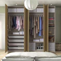 an open closet with clothes hanging on the walls and drawers in front of it, next to a bed